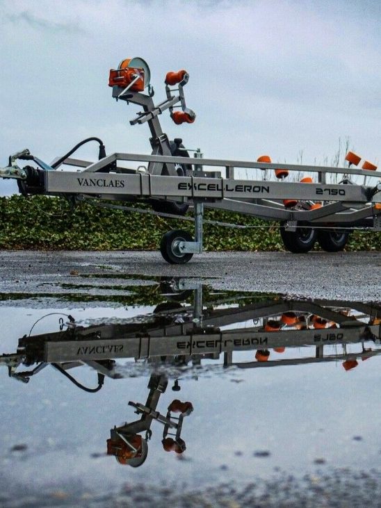 Vanclaes Exceleron Bootstrailer auf nasser Straße mit Spiegelung, umgeben von Vegetation