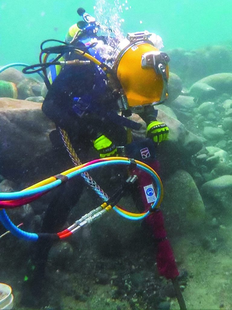 Taucher mit hydraulischem Abbruchhammer von HYCON unter Wasser, umgeben von Felsen und Kabeln