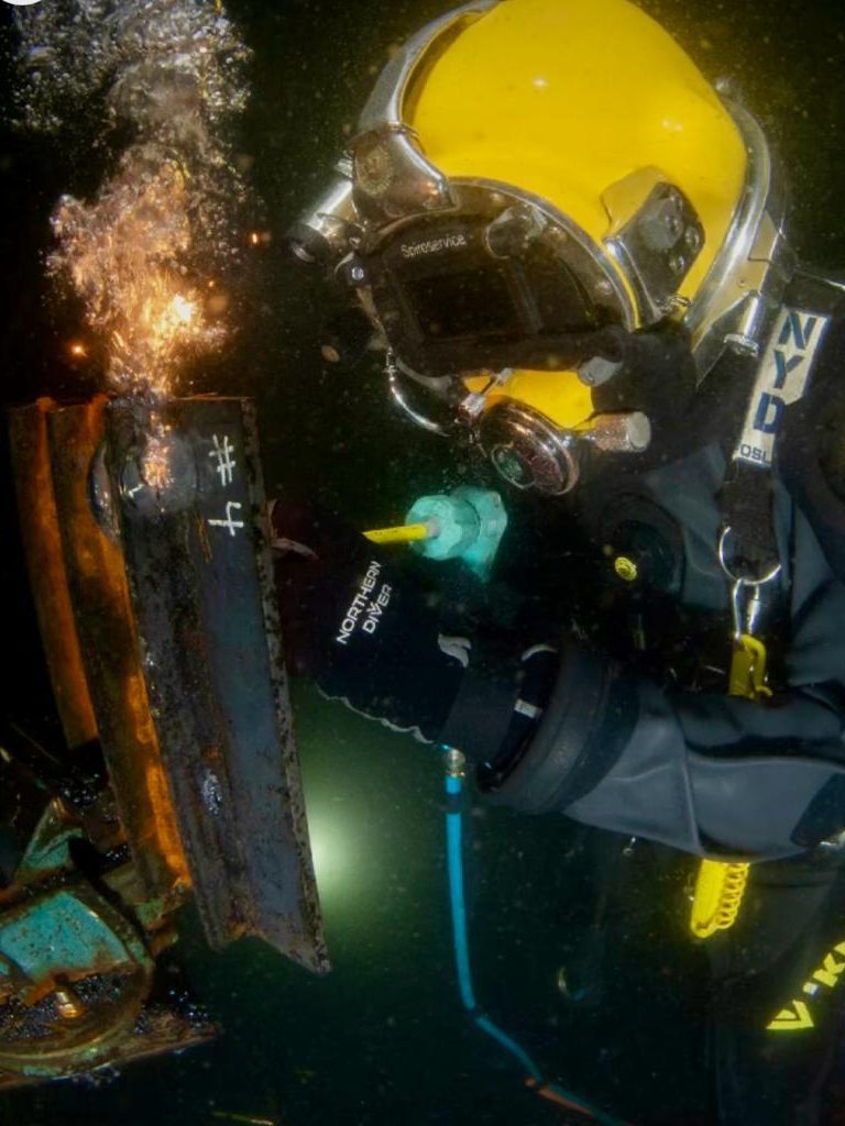 Taucher unter Wasser beim Brennschneiden eines Metallstücks, Funken sprühen durch den Brenner