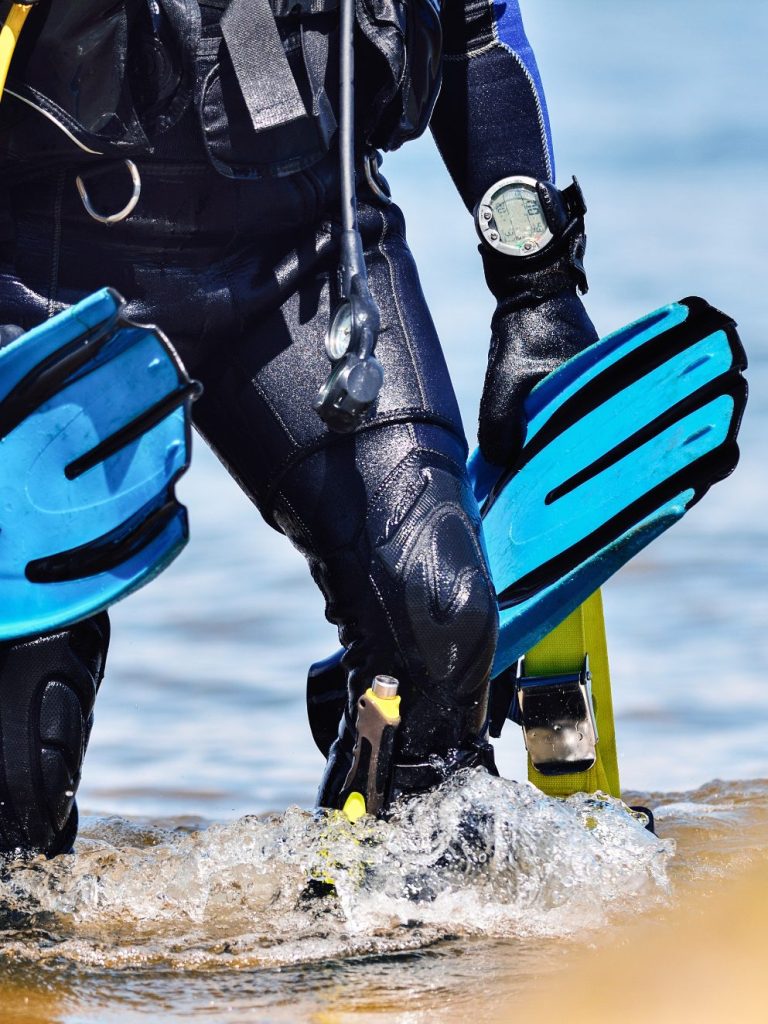 Professioneller Taucher geht mit blauen Flossen und vollständiger Ausrüstung aus dem Wasser